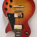 Elektrická kytara s tělem v červeno-žlutém gradientu (sunburst) a viditelnou strukturou dřeva. Nástroj má zlatý hardware, dva humbuckery a čtyři čern…