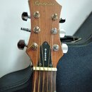 Hlava akustické kytary z hnědého dřeva s nápisem Epiphone. Na černé hranici hmatníku je viditelný vertikální nápis GIBSON. Nástroj má šest kovových l…