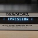 Stříbrný rackový procesor s nápisem ROCKTRON TECHNOLOGY FOR GUITARISTS. Na displeji je zobrazen text 1 XPRESSION 1. Zařízení má ovládací knoflíky a t…
