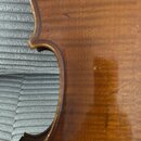 Detailní záběr na hranu hřísta smyčcového nástroje z lakovaného dřeva v hnědé barvě. Povrch vykazuje drobné škrábance a opotřebení laku. Žádné značky…
