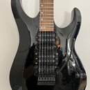 Černá elektrická kytara s hnědým hmatníkem. Nástroj má dva humbuckery a tremolo mechanismus, na kterém je viditelný nápis Cort. Povrch kytary je lesk…