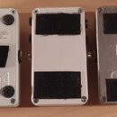 Pět kytarových efektů z pohledu spodu. První, čtvrtý a pátý pedal mají stříbrné kovové šasi, druhý a třetí jsou bílá. Na spodní stranách jsou černé s…