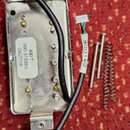 Kovová elektronická součástka s černým kabelem a bílým konektorem. Na bílé nálepce je text 490 T, 866-51939-L a 09/27/118, na kabelu je nápis BRIDGE.…