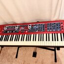 Červený digitální klavír Nord Stage 3 umístěný na černém stojanu. Na levé straně je bílý nápis nord Stage 3 a pod ním menší text ORGAN PIANO SYNTH SE…