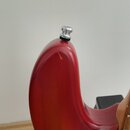 Detail zadní strany červené kytary s kovovým popruhovým háčkem na horním okraji těla. Lak v oblasti nad hřidnem vykazuje viditelné odřapání a opotřeb…