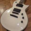Bílá elektrická kytara s tvarem připomínajícím model Les Paul. Nástroj má dva černá humbuckery, tři černé ovládací knoflíky a jeden přepínač. Na těle…