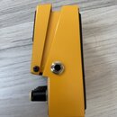 Žlutý kytarový efekt v kovovém šasi. Na boku je vidět jeden vstupní/výstupní jack konektor a část černého ovládacího knoflíka. Povrch je hladký bez v…