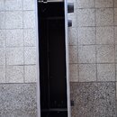 Otevřený hliníkový transportní kufr s černým vnitřním povrchem. Má stříbrné kovové hrany a čtyři černé plastové nožky na jedné straně. Na koncích jso…