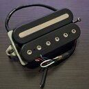 Černý humbucker s dvěma cívkami a kovovým krytem v horní části. Spodní cívka má šest viditelných polových šroubů. Nástroj je umístěn na kovové základ…