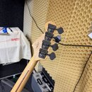 Záběr na hlavu a hřbet krku basové kytary z přírodního dřeva. Na zadní straně hlavy je vidět podpis „Leo Fender“. Nástroj má čtyři černé ladicí mecha…