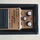 Zlatý kytarový pedál značky BOSS s nápisem Acoustic Preamp AD-2, umístěný v černé krabici. Na horní straně jsou tři bílé ovládací knoflíky s popisky…