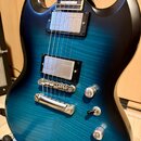 Elektrická kytara s modrým gradientním lakem a viditelnou strukturou dřeva. Nástroj má dva humbuckery s kovovými kryty, stříbrný most a tři ovládací…