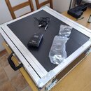 Na černé ploše hliníkového transportního kufru leží dva černé bezdrátové vysílače značky TecBone. Na obou je viditelný nápis „TecBone free 5000 PT 82…