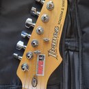 Hlava elektrické kytary z přírodního dřeva s chromovanými ladičkami. Na povrchu je černý nápis Ibanez a text THE ULTIMATE EXPRESSION OF CRAFTSMANSHIP…