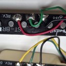 Černý elektrický kytarový snímač s šesti kovovými póly. Na povrchu je bílá nálepka s nápisem ST-BR S a vpravo cursivem napsané logo Fender. V horní č…