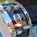 Černý buben s chromovaným obručováním a ladicími šrouby. Na korpusu je viditelný štítek s nápisy YAMAHA a GIGMAKER. V horní části pozadí je vidět čás…