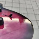 Detail korpusu elektrické kytary s fialovým gradientem a tmavým okrajem. Na povrchu jsou vidět dva černé ovládací knofíky a jeden černý přepínač. Lak…