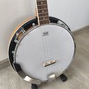 Bílá membrána banjona s nápisem REMO WEATHERKING BANJO HEAD ONLY. Nástroj má kovový chromovaný rám a hnědý dřevěný krk s hvězdicovými značkami na hma…