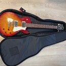 Elektrická kytara s červeně-žlutým sunburst povrchem těla a bílým pickguardem, položená v otevřeném černém softcase. Na hlavě kytary je viditelné log…