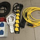 Sada elektrických prodlužovacích kabelů a rozdělovačů v různých provedeních. Je zde černý a žlutý kabel, bílá zásuvková lišta s třemi hnízdy a černá…