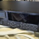 Černý rackový digitální nahrávací zařízení s nápisem ALESIS MERLINLINE ML-8000 HIGH-RESOLUTION MASTER DISK RECORDER. Přední panel obsahuje displej, ř…