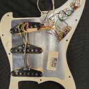 Bílá pickguard s instalovanou elektronikou a třemi humbuckery. Na snímačích jsou ručně napsaná čísla 131, 132 a 133. Na bílé nálepce je čárcový kód a…