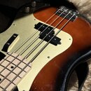 Detail elektrické basové kytary s tělem v provedení sunburst. Nástroj má zlatý plech (pickguard), dva černé snímače a čtyři struny. Na povrchu laku j…