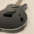 Černá elektrická kytara s bílým lemováním kolem těla. Nástroj má dva humbuckery, jeden ovládací knoflík a přepínač zvuků. Na těle nejsou viditelné žá…