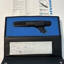 Černý dynamický mikrofon s držákem, umístěný v modrém pěnovém vložce černého kufru. Na těle mikrofonu je bílý nápis SENNHEISER. Součástí je dokumenta…