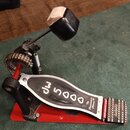 Červený basový pedál s kovovou stupňovací deskou. Na desce je nápis „dw 5000“ a menší text „The Drummer's Classic ®“. Pedál vykazuje známky používání…
