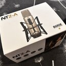 Bílá čtvercová krabice s nápisem NT2-A MULTI-PATTERN STUDIO CONDENSER MICROPHONE a logem RØDE MICROPHONES. Na krabici je zobrazen stříbrný kondenzáto…