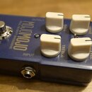 Modrý kytarový efekt s bílými ovládacími knoflíky. Na šasi jsou nápisy tc electronic, MOJOMOJO a PAUL GILBERT OVERDRIVE. Viditelné popisky u knoflíků…