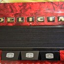 Detail akordeonu s červeným mramorovaným povrchem. V horní části je nápis DELICIA tvořený zlatými písmeny v černých čtvercových rámečcích. Střední čá…