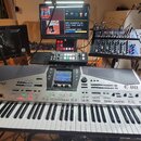 Stříbrný klavír Roland E-80 s displejem a ovládacími prvky v horní části. Nad nástrojem je umístěn mixážní pult, kontroler a monitor s textem WWW.HAG…