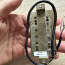 Detailní pohled na zadní stranu kytarového snímače v kovovém krytu s viditelnou korozí a opotřebením povrchu. Na kovovém krytu je vyražen nápis „Styr…