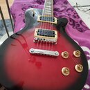 Elektrická kytara s červeným gradientem (sunburst) a černým pickguardem. Na snímačích je viditelný nápis INF4. Kytara má čtyři zlaté ovládací knofíky…
