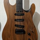 Elektrická kytara s tělem a hnedkem z tmavého dřeva. Na hmatníku je bílé logo ve tvaru symbolu nekonečna. Kytara má tři černé humbuckery s nápisem Se…