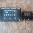 Na fotografii je černý kytarový efektový procesor Boss GT-1000core a jeho originální kartonová krabice. Na přístroji i na krabici je vidět nápis BOSS…