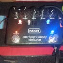 Černý efekt pedál s nápisy MXR a carbon copy deluxe. Na horní straně jsou pětiknobové ovladače s popisky MIX, REGEN, DELAY, SPEED a WIDTH. Jsou zde t…