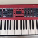Červený digitální klavír s bílými a černými klávesami. Na pravé straně je bílý nápis nord piano 5 a pod ním menší text VIRTUAL HAMMER ACTION TECHNOLO…