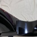 Detailní záběr na černý lakovaný korpus kytary. Na spodní hraně je vidět jeden kovový ladicí kolík nebo šroub. Povrch laku je lesklý s viditelnými od…