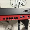 Zadní strana červeného elektronického nástroje s černým horním krytem. Jsou zde viditelné vstupy a výstupy s nápisy INPUT 2, INPUT 1, GAIN 1 (s přepí…