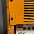 Detail žlutého kytarového zesilovače s ventilační mřížkou. Na spodním panelu jsou nápisy MADE IN BRITAIN s britskou vlajkou, SWITCHES a popisky konek…