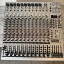 Stříbrný mixážní pult s mnoha ovládacími prvky a posuvníky. V pravém horním rohu je nápis EUROBRACK UB2442FX-PRO a logo BEHRINGER. V horní části jsou…