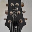 Černá hlava kytary s nápisy Paul Reed Smith SE a CE. Jsou na ní vidět šest chromovaných ladiček. Povrch je matný a v dobrém stavu.
