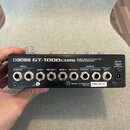 Zadní strana černého efektového procesoru s nápisem BOSS GT-1000CORE GUITAR EFFECTS PROCESSOR. Jsou zde vidět vstupy a výstupy s označením INPUT (R/M…