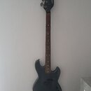 Tmavě šedá elektrická basová kytara s hnědým hmatníkem. Na hlavě je svisle napsáno „proxima t-bass“. Tělo nástroje vykazuje známky opotřebení v podob…