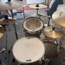 Krytá bicí souprava s několika cymbally a bubny. Na bubnech jsou viditelné loga TAMA a EVANS. Cymbally nesou nápis Zildjian. Povrchy nástrojů jsou v…