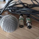 Dynamický mikrofon s kovovou síťovkou a dvěma XLR konektory na černých kabelech. Na těle mikrofonu je částečně viditelný bílý nápis „LS 8“. Konektory…