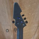 Fotografie zachycuje hlavu kytary s černým povrchem imitujícím karbonová vlákna. Na hlavě jsou umístěny čtyři ladicí mechanismy s černými knoflíky. N…